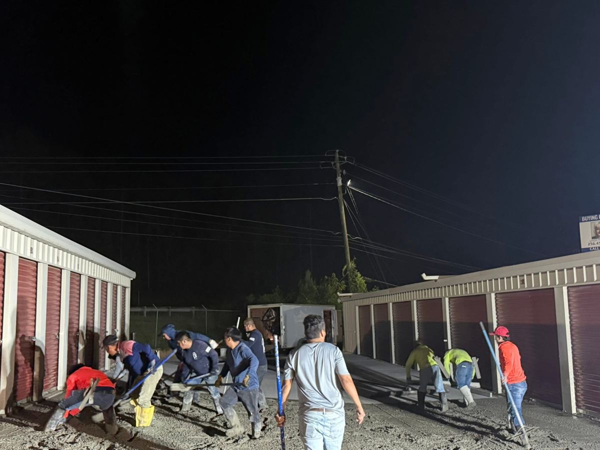 A big crew pouring concrete at night under lights
