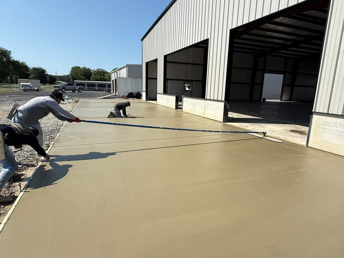 Crew screeding a fresh slab in front of a steel building